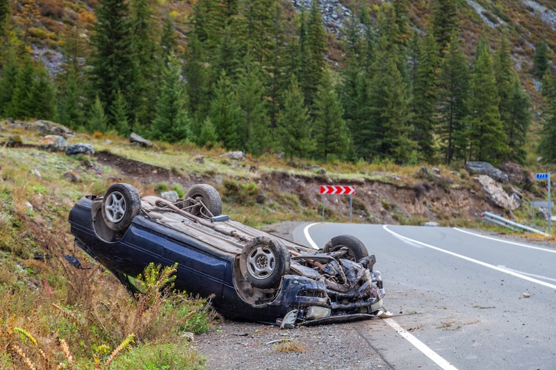 Car accident place on a bend, overturned car lies on the roof, broken bumper, glass, mountain road