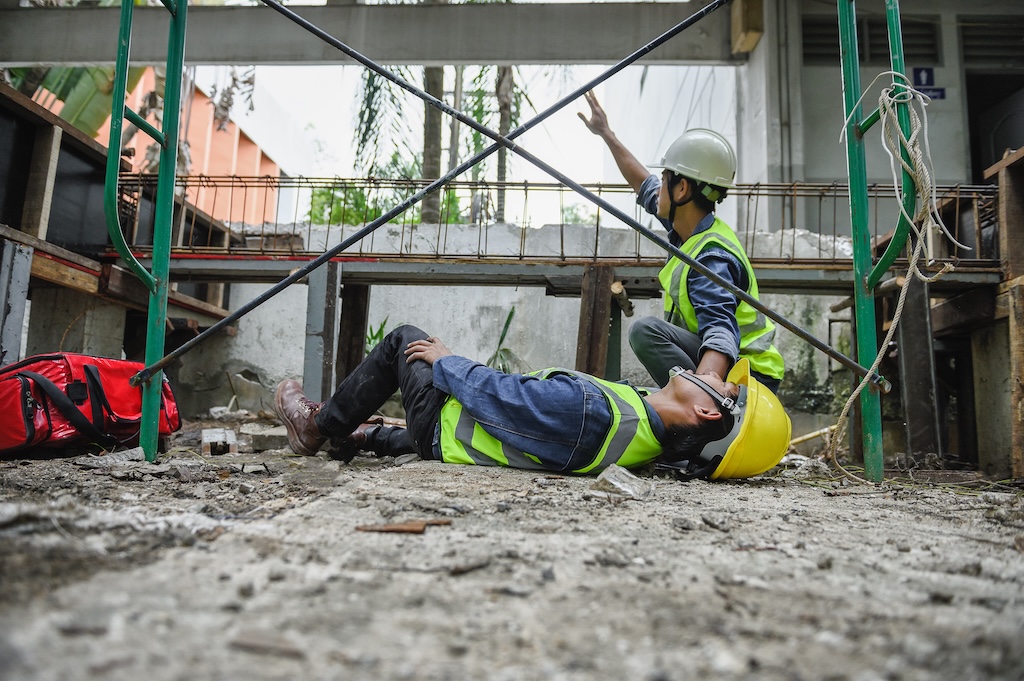 First aid support accident at work of builder worker in construction site. Accident falls from the scaffolding on floor, Foreman help employee accident with first aid bag and wave hand to team help. Slip and Fall