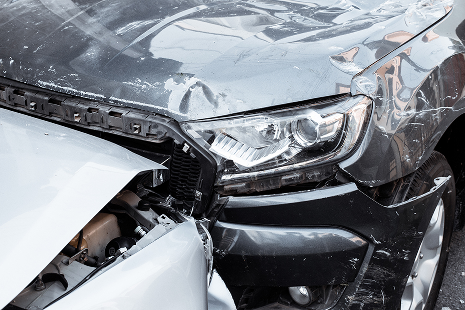 Front-left crash damage showing a dented hood, exposed engine bay, and damaged bumper on a silver car after a collision