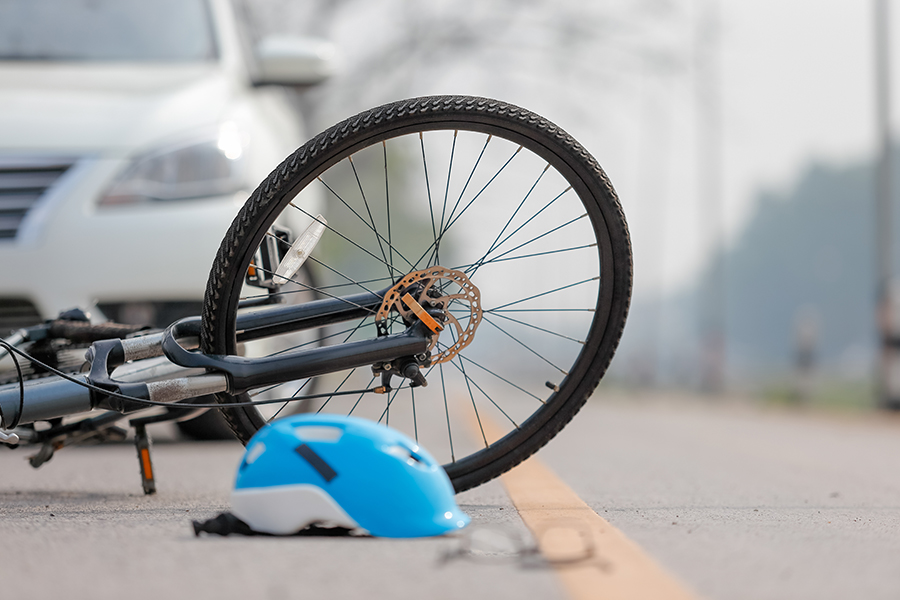Bicycle lying on its side on a street with a blue helmet on the road in the foreground and a white car in the background.